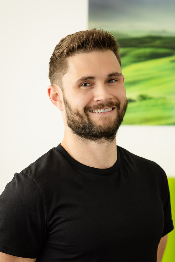 Hauptbild eines jungen männlichen Physiotherapeuten in Praxis, lächelnd und freundlich.