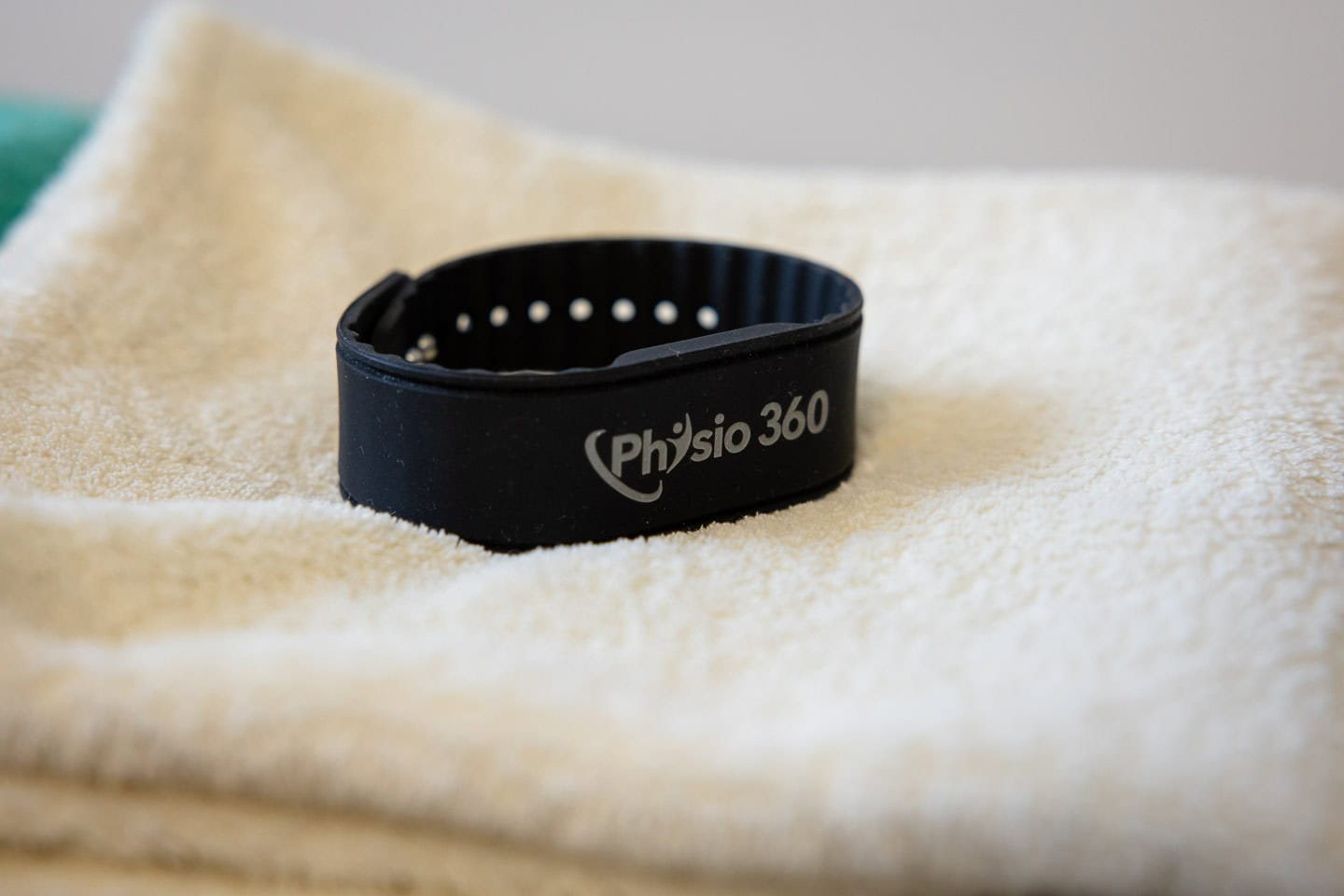 Schwarzarmband mit "Physio 360" Logo auf weichem Handtuch.