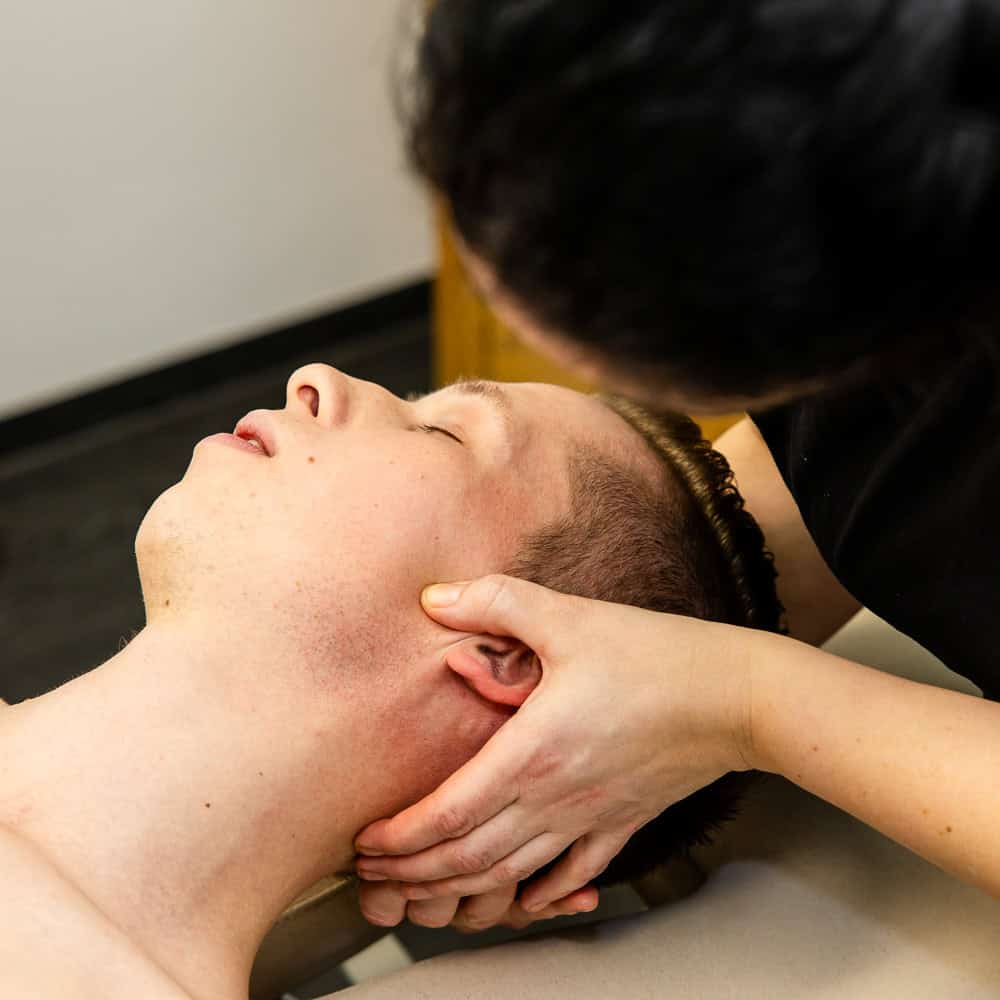 Physiotherapeutin behandelt Nackenbereich eines Patienten bei Physiotherapie in Penzberg.