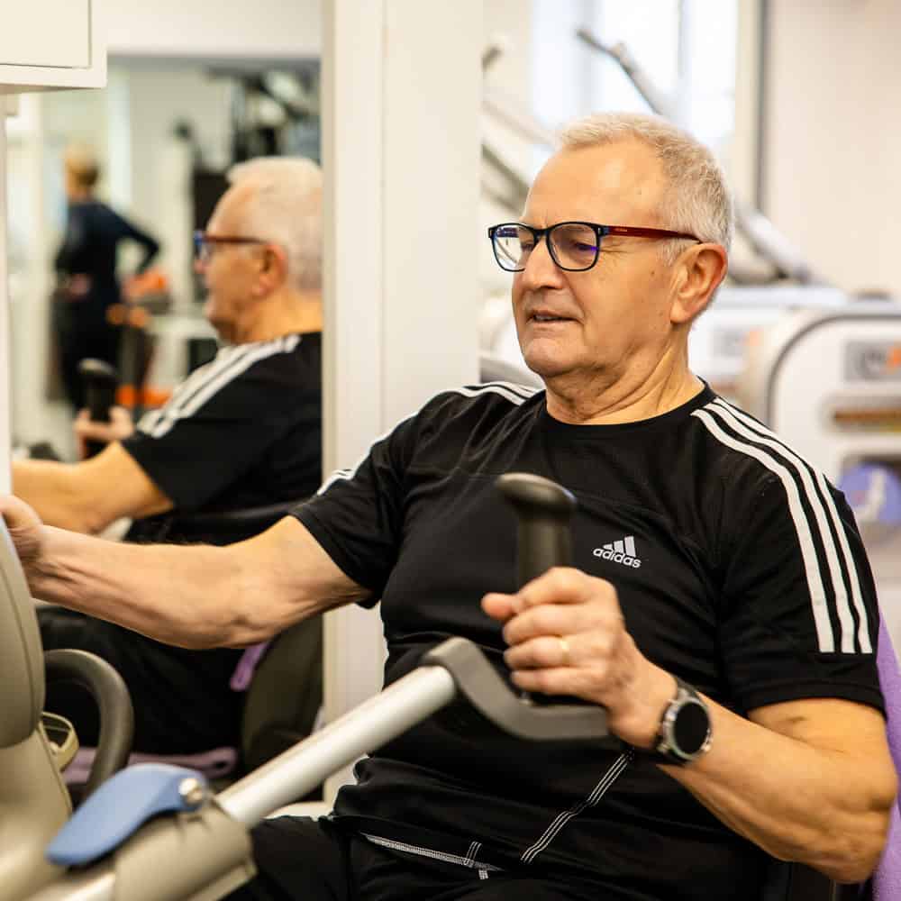 Älterer Mann trainiert im Fitnessstudio mit Hanteln, Fokus auf Kraft und Gesundheit.