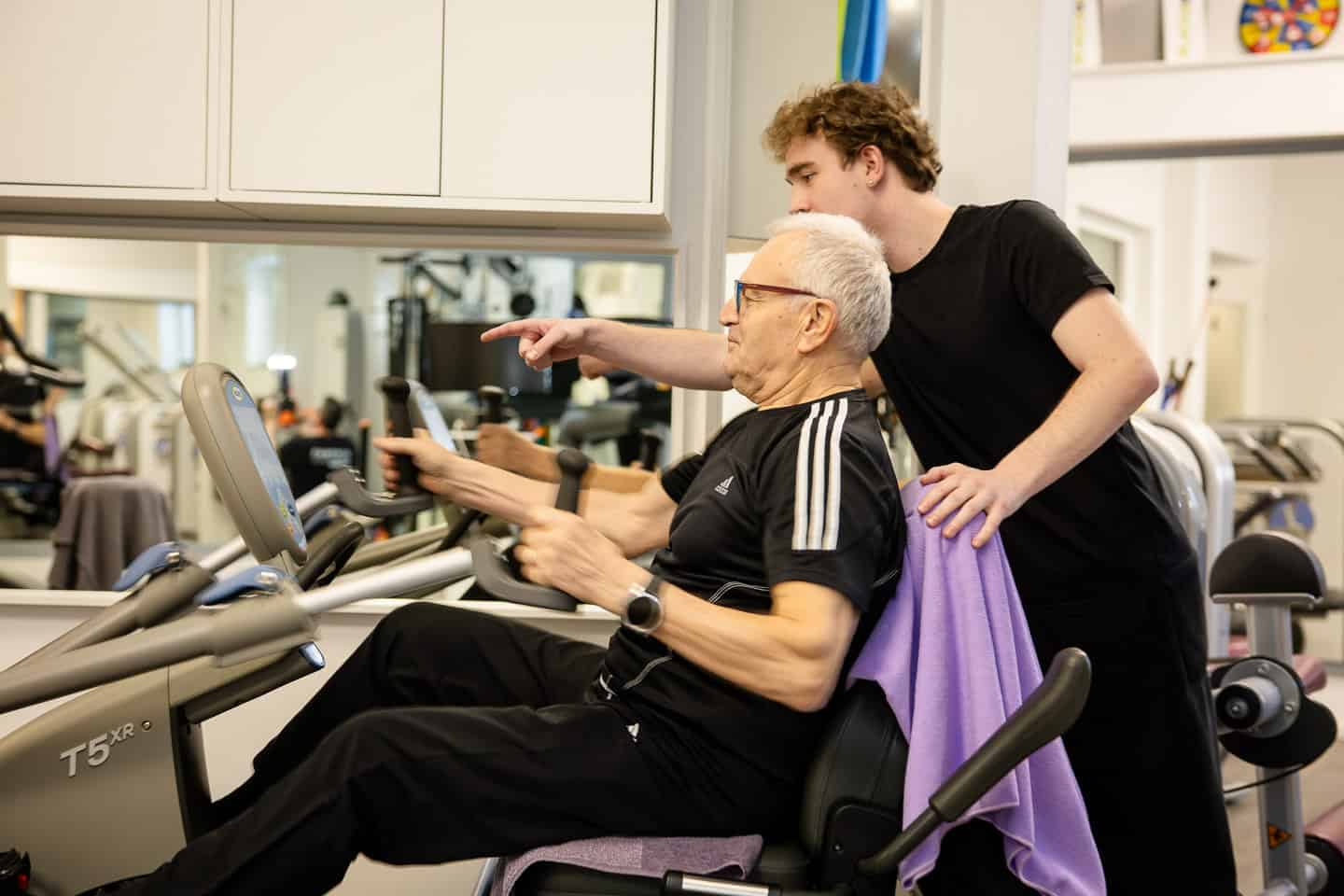 Physiotherapie bei älterer Frau im Fitnessstudio, betreut von Trainer.