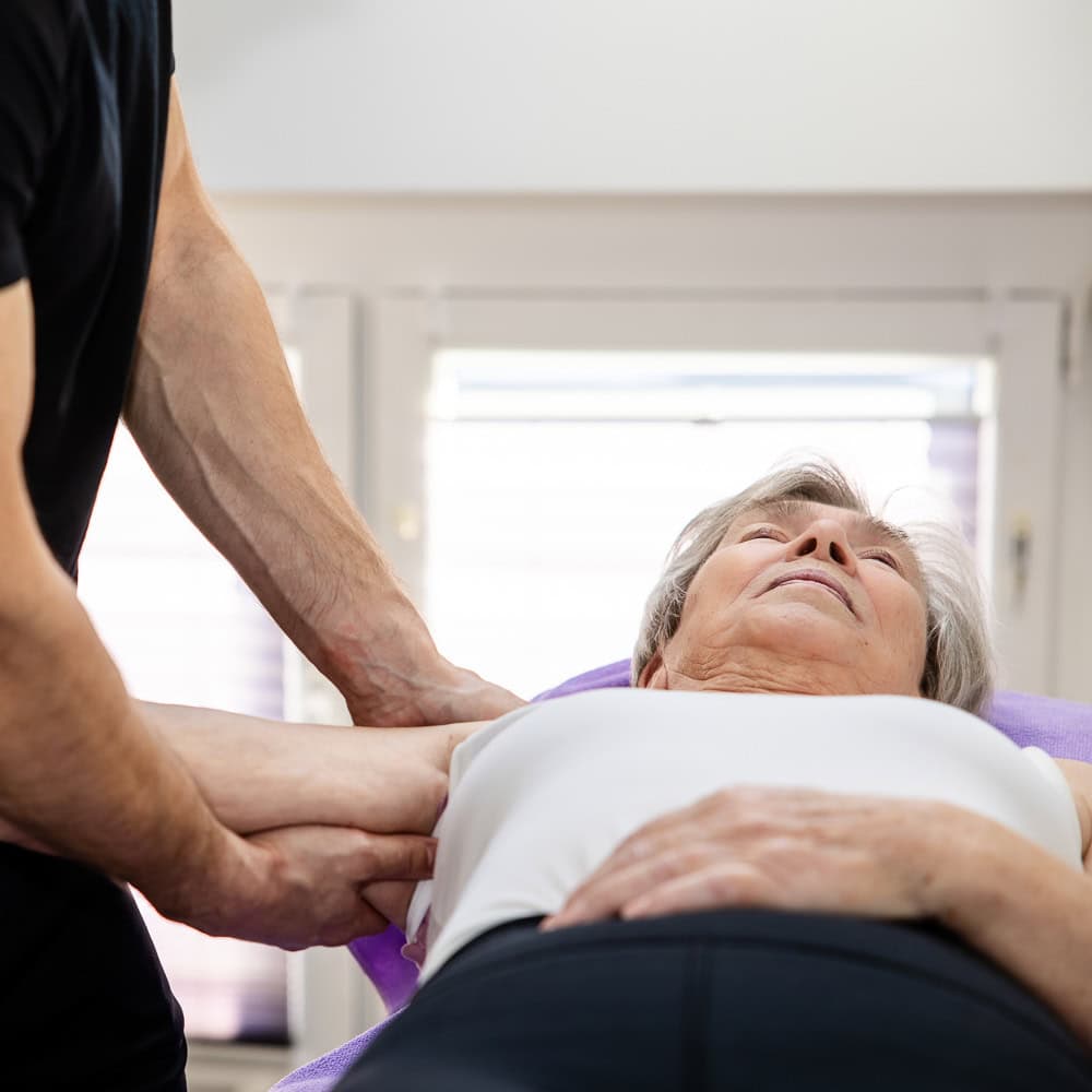 Physiotherapeut behandelt ältere Patientin bei Physiotherapie in Penzberg.