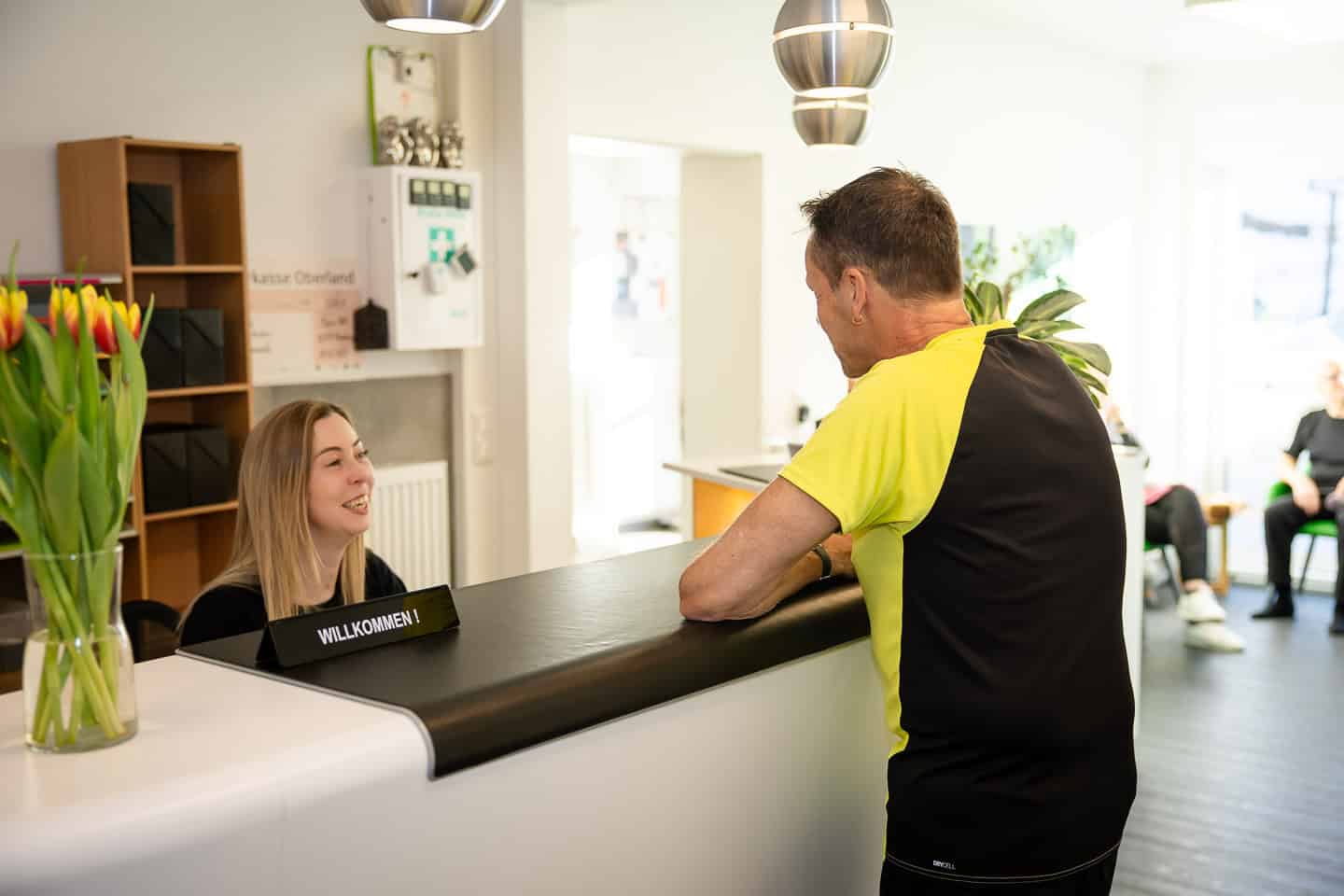 Freundliches Gespräch zwischen Patient und Physiotherapeut an der Rezeption.